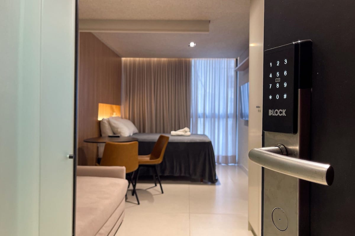 Una habitación de hotel moderna con cama, escritorio, silla, sofá y puerta con cerradura electrónica.