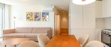 Una sala de estar moderna con una mesa de comedor de madera, un sofá color beige y una cocina con gabinetes blancos y una estufa.