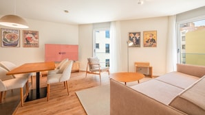 Un salon moderne avec une table à manger en bois, des canapés beiges et une grande fenêtre donnant sur des immeubles.