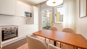 Una cocina moderna con armarios blancos, horno empotrado y un comedor con mesa y sillas de madera.