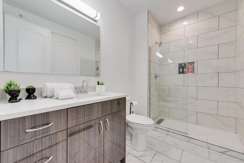 A modern bathroom with a white vanity, a large mirror, a glass shower enclosure, and a toilet.