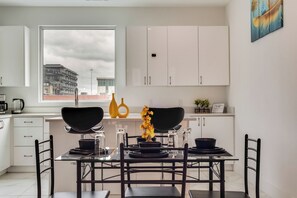 A modern kitchen with white cabinets, a dining table with black chairs, and a window with a city view. - Dallas City Views  (Dallas)