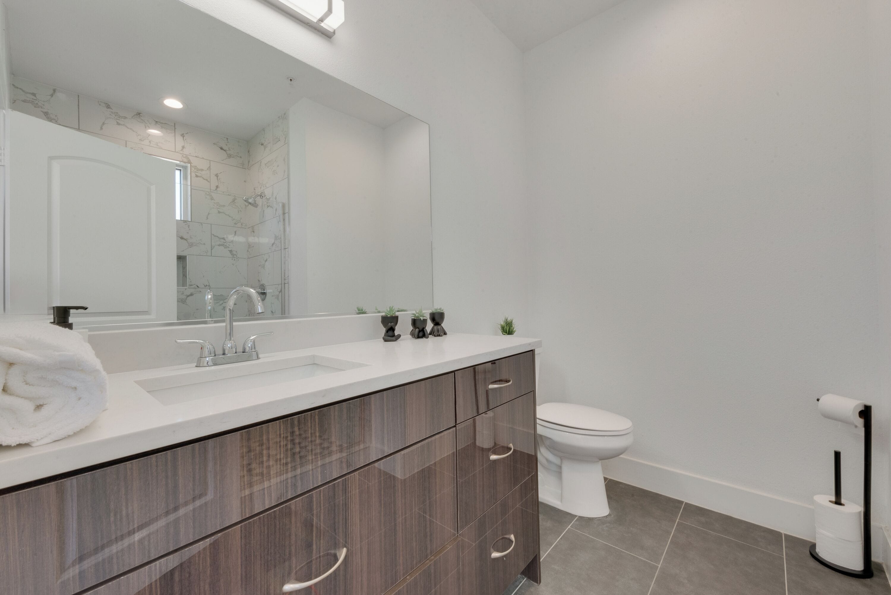 Une salle de bain moderne avec un pare-baignoire en marbre, un lavabo blanc, un meuble-lavabo en bois foncé et des toilettes.