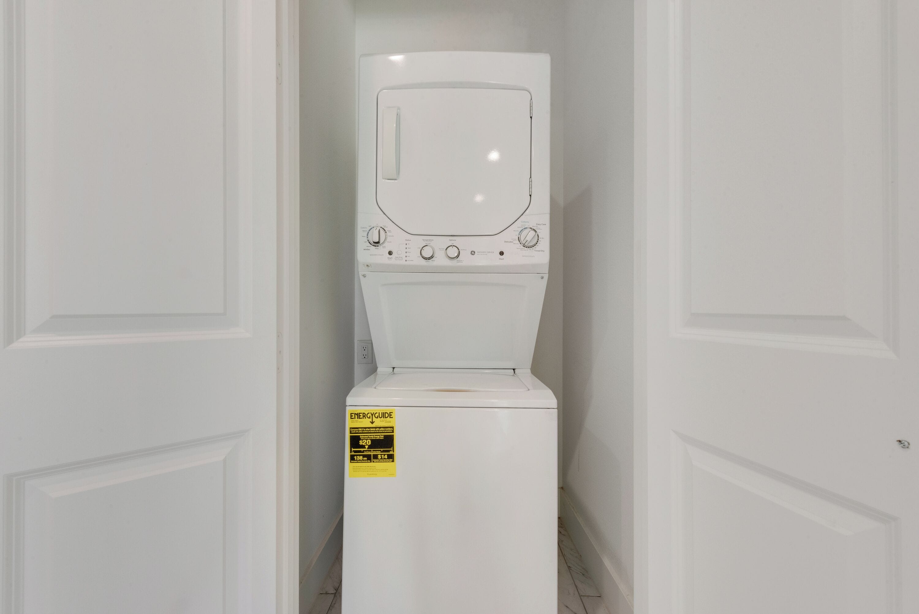Une machine à laver blanche se trouve dans un couloir étroit, avec des portes blanches de chaque côté.