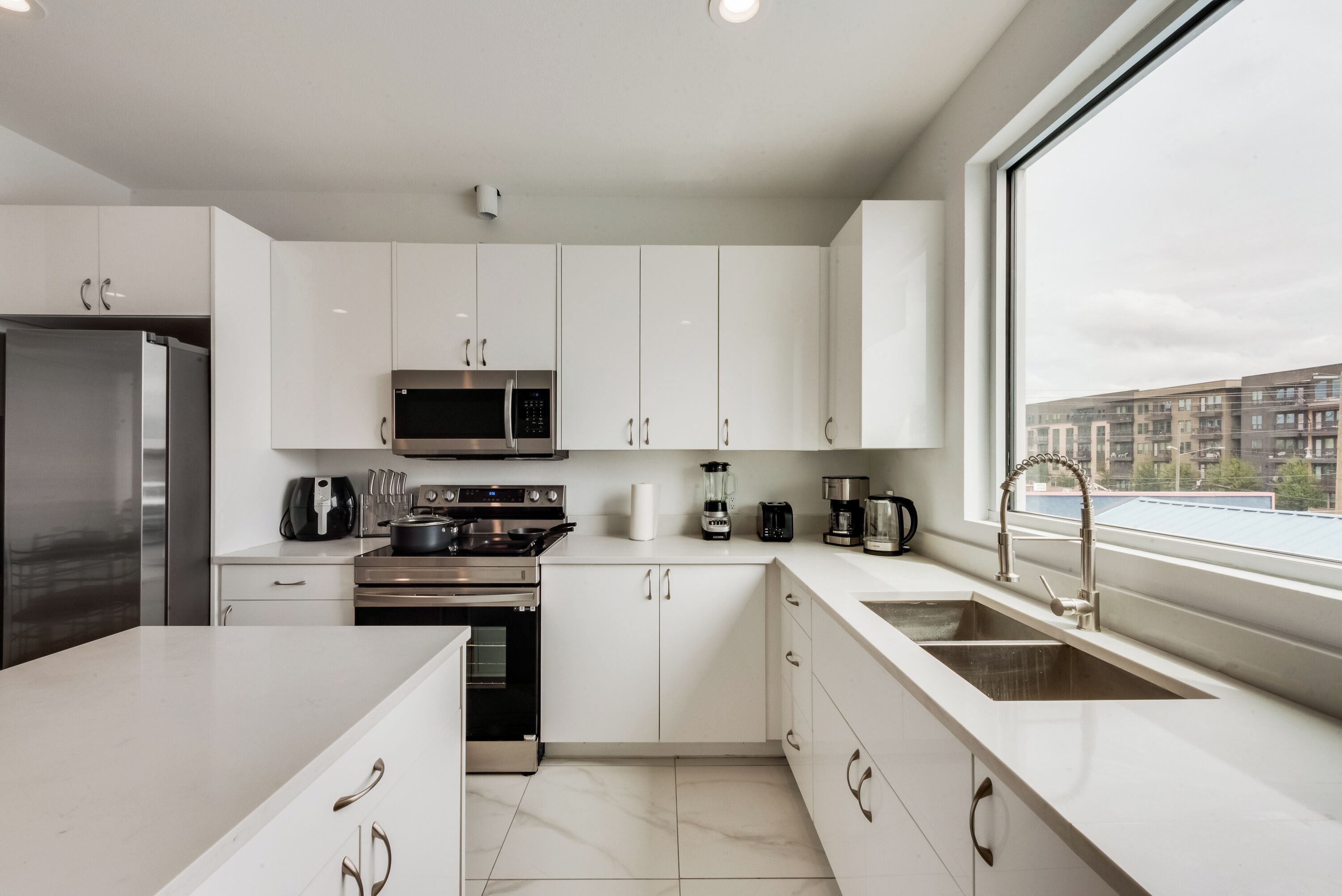 A modern kitchen with white cabinets, stainless steel appliances, and a large window offering a view of the cityscape.
