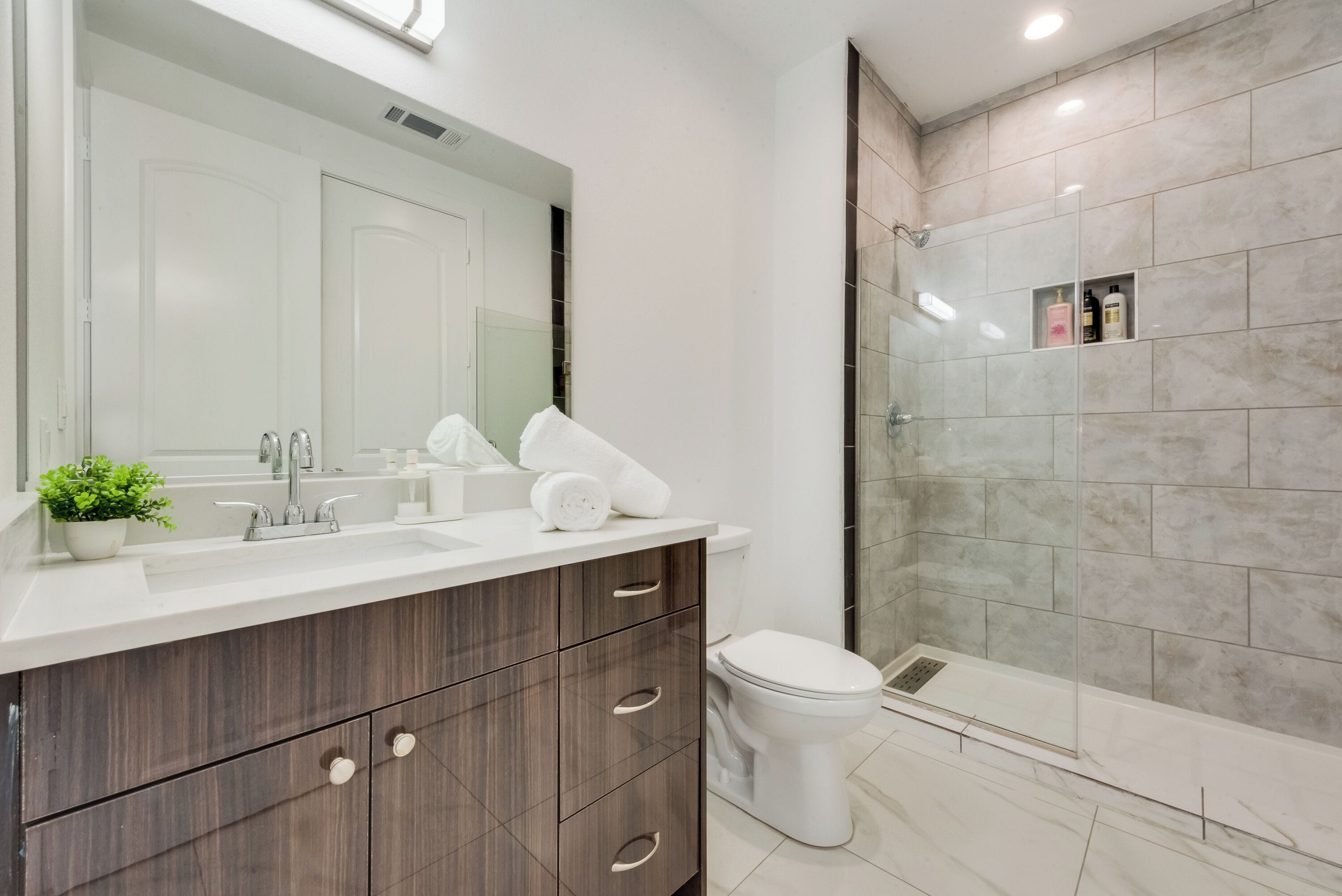 A modern bathroom with a large mirror, a sink with a towel holder, a toilet, and a glass-enclosed shower area.