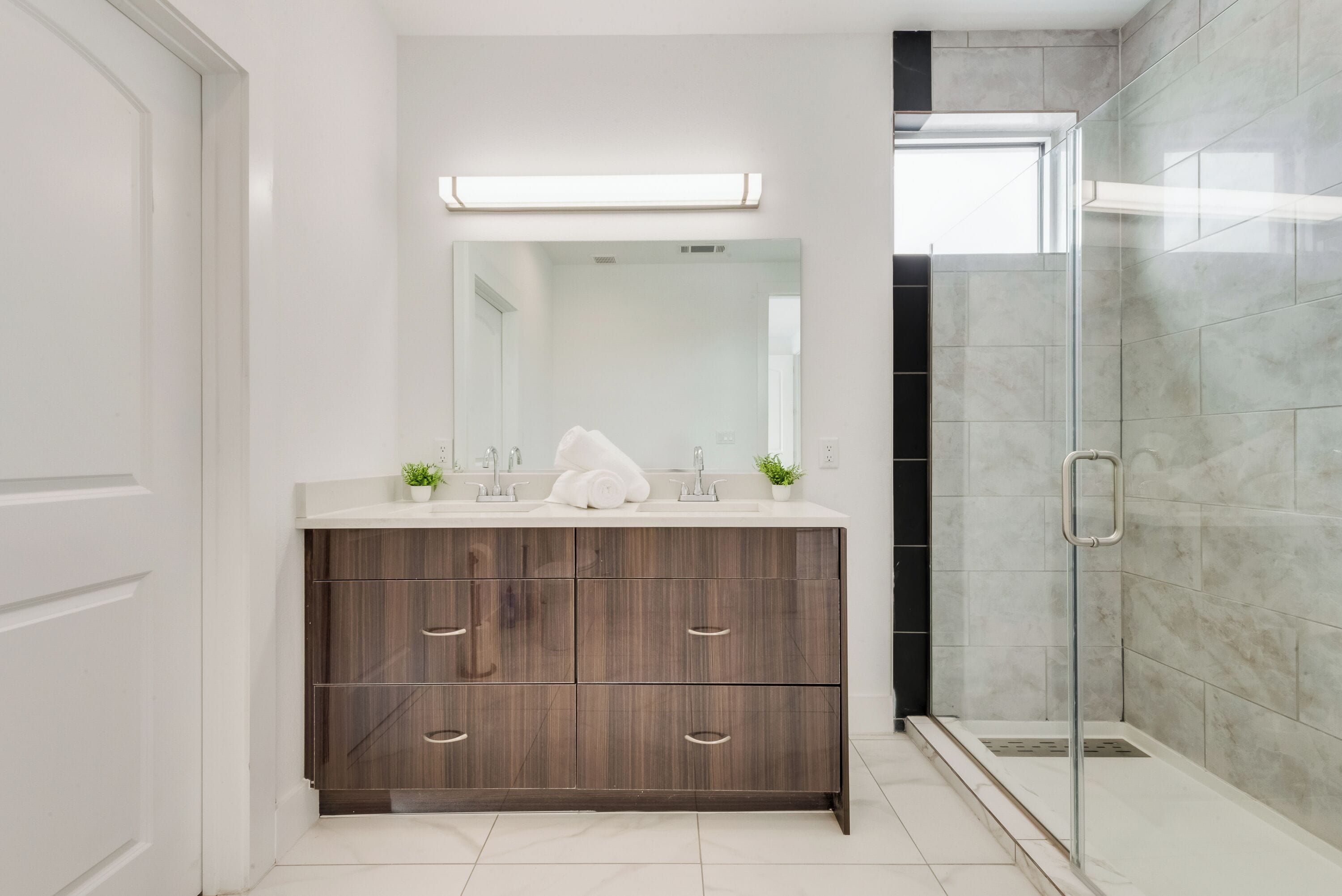 Ein modernes Badezimmer mit einem Holzbadezimmer-Möbel, einem großen Spiegel und einer Duschkabine aus Glas.