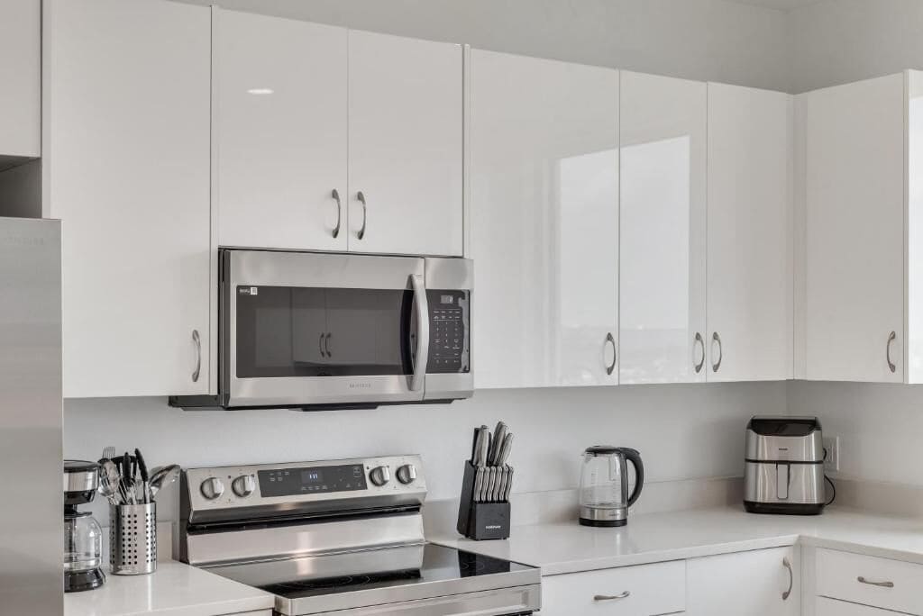 A modern kitchen with white cabinets, a stainless steel microwave, an oven, a coffee maker, and a toaster.