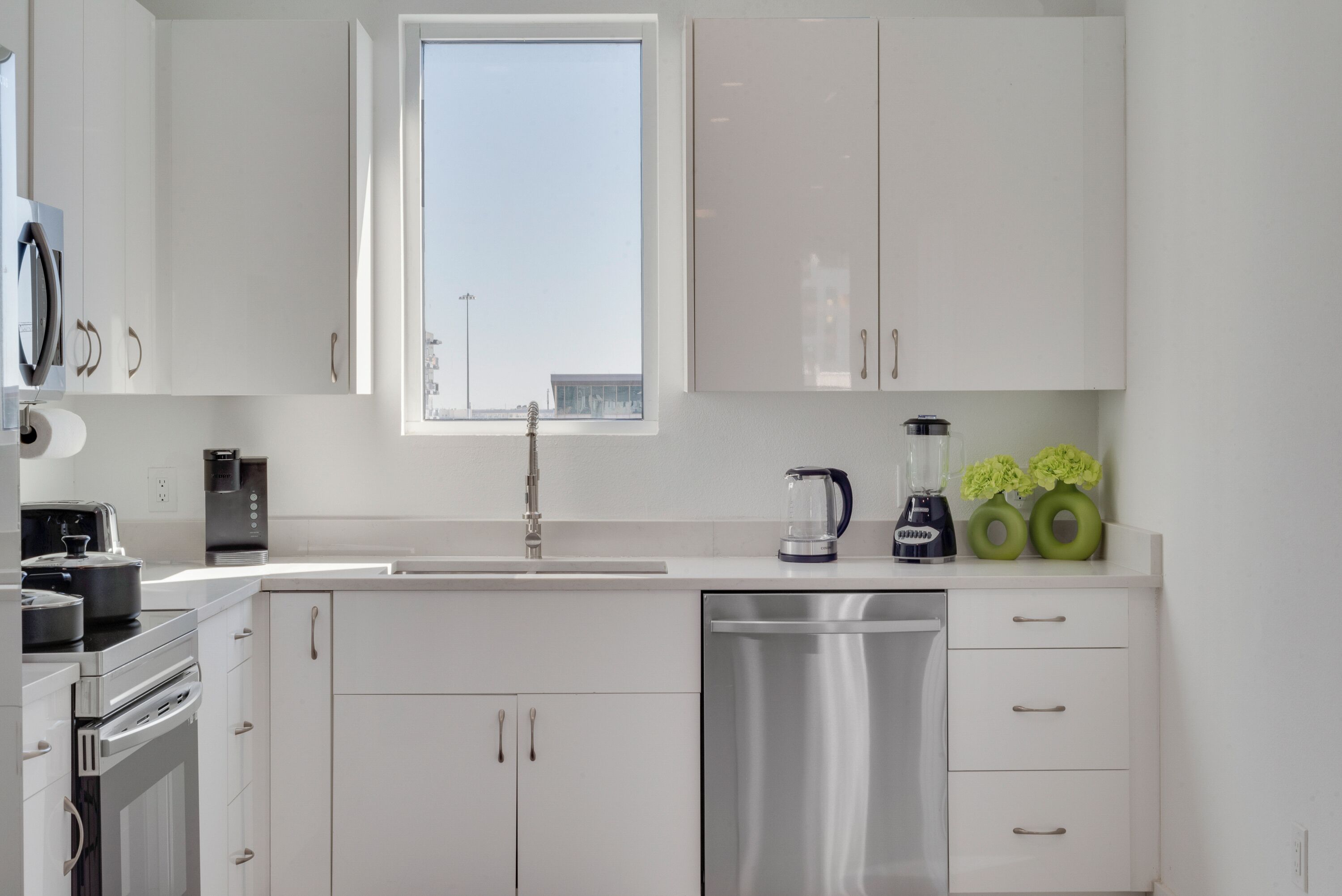 A modern kitchen with white cabinets, a stainless steel dishwasher, a coffee maker, and a blender.