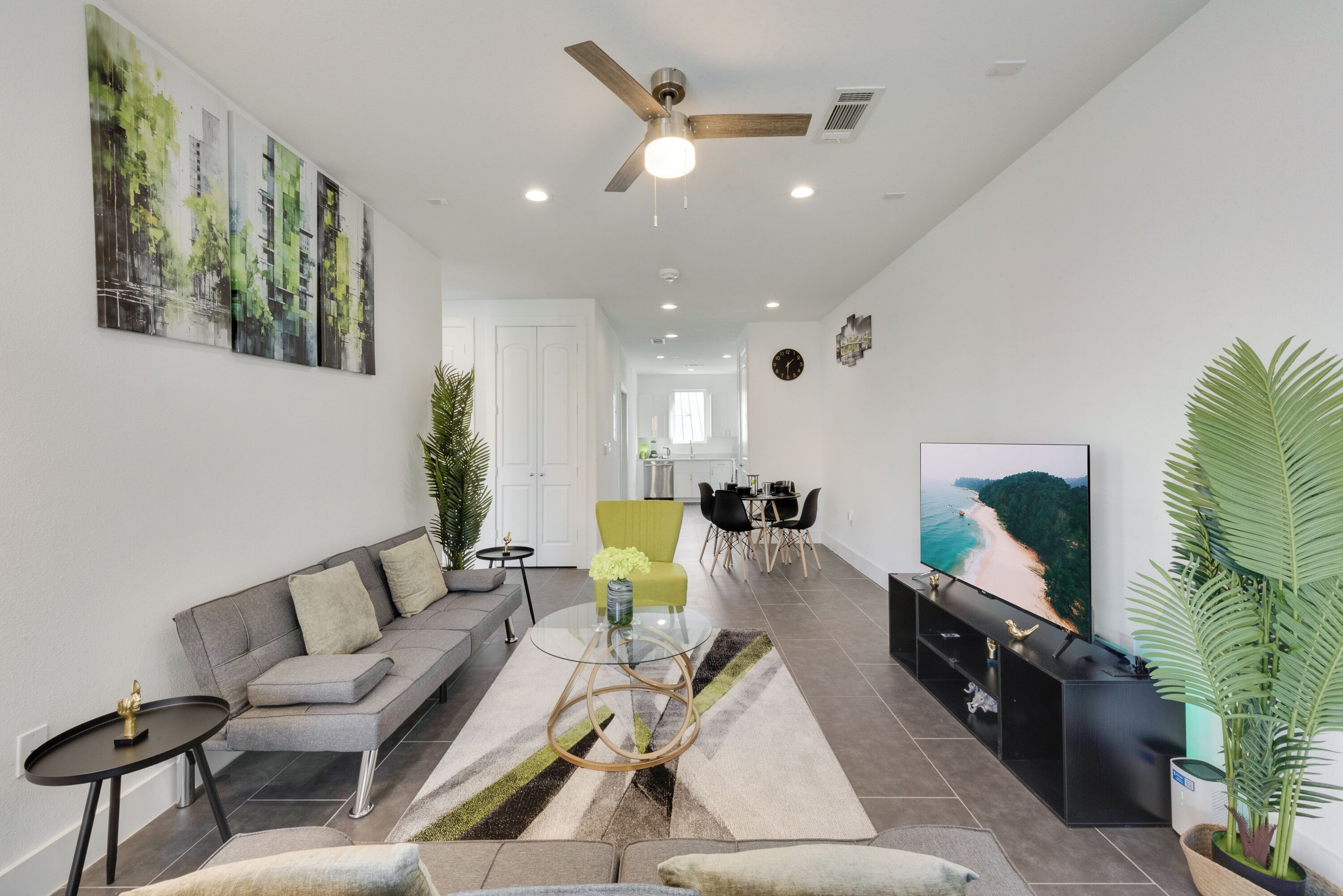 A modern living room with a grey sofa, a glass coffee table, and a TV on a black stand.