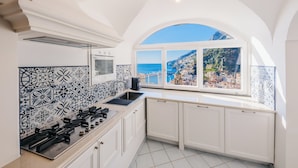 Une cuisine avec des meubles blancs, une cuisinière à gaz et une vue sur une ville côtière, visible à travers une grande fenêtre en arc de cercle.