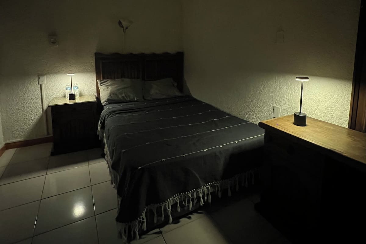 A bedroom with a bed, two bedside tables, a nightstand, a lamp, and a wall-mounted light fixture.