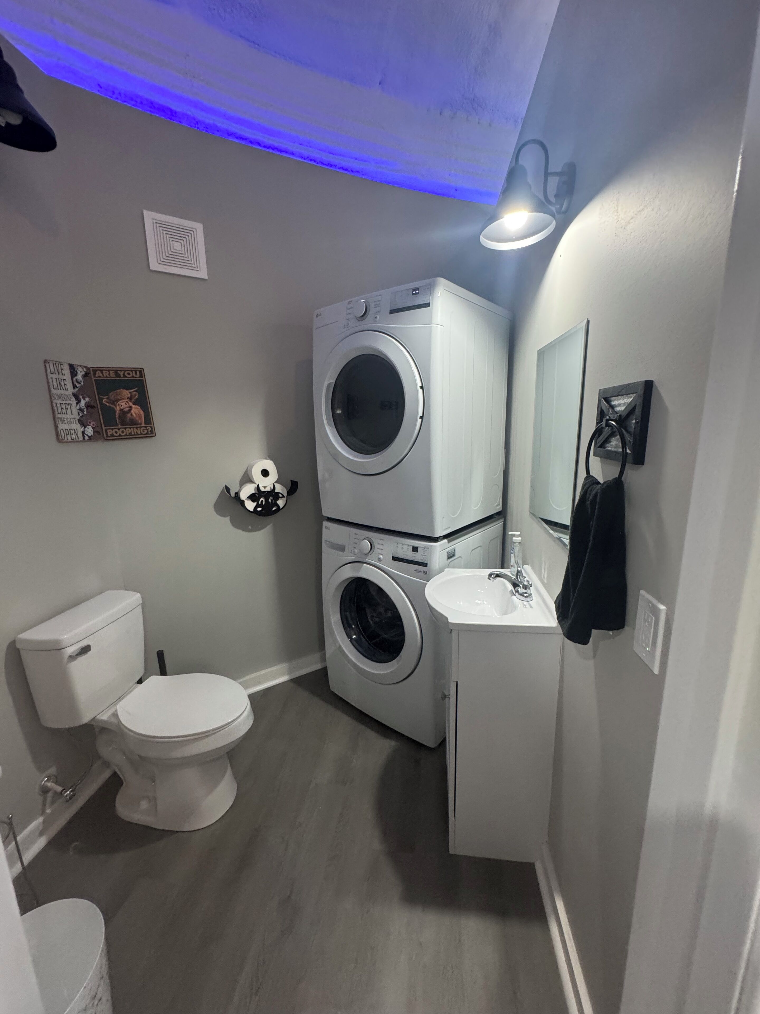 Un baño pequeño con inodoro, lavadora-secadora doble, lavabo y espejo.