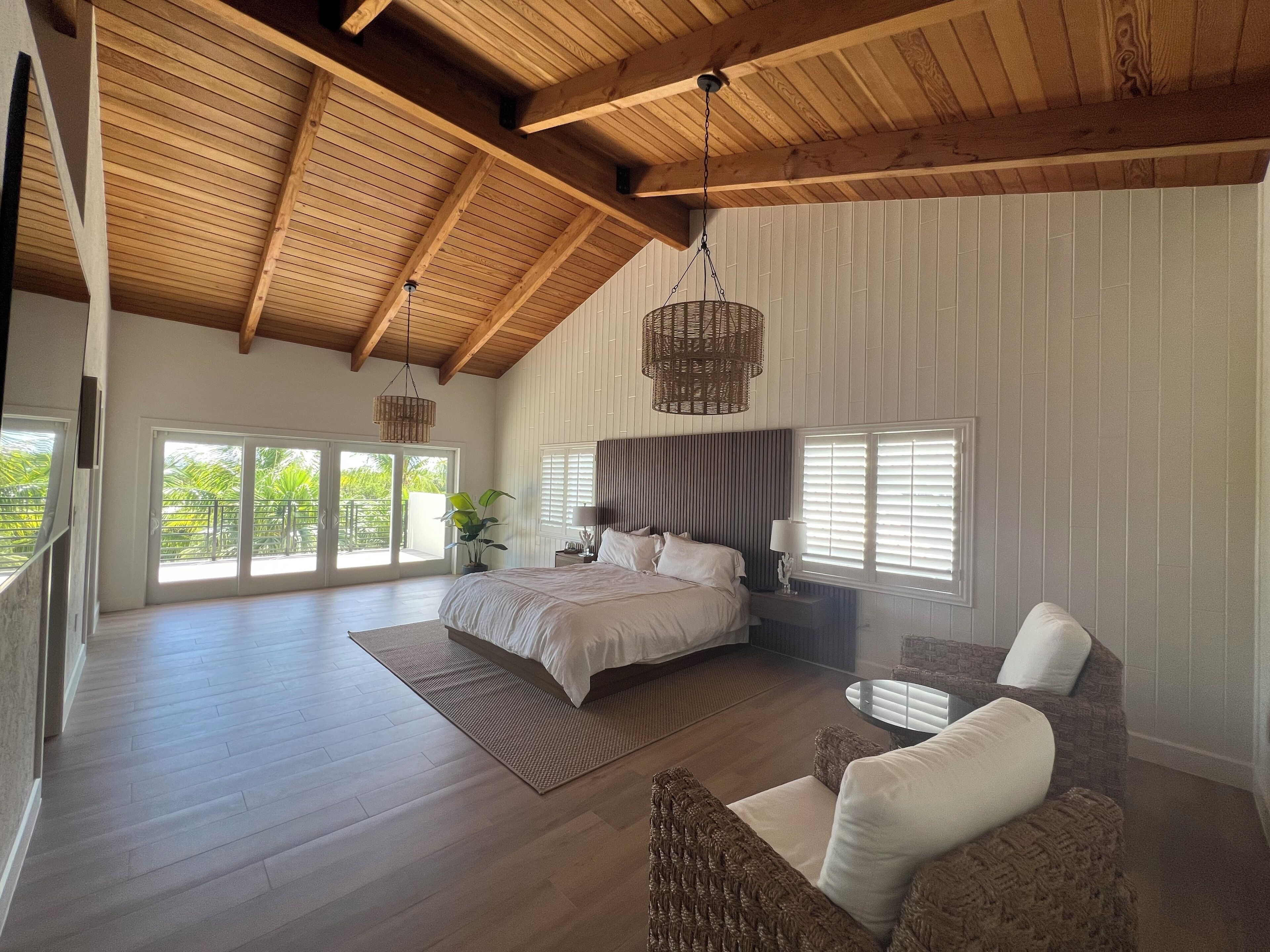 Un dormitorio amplio con una cama grande, una zona de estar con una silla y un balcón con puertas correderas.