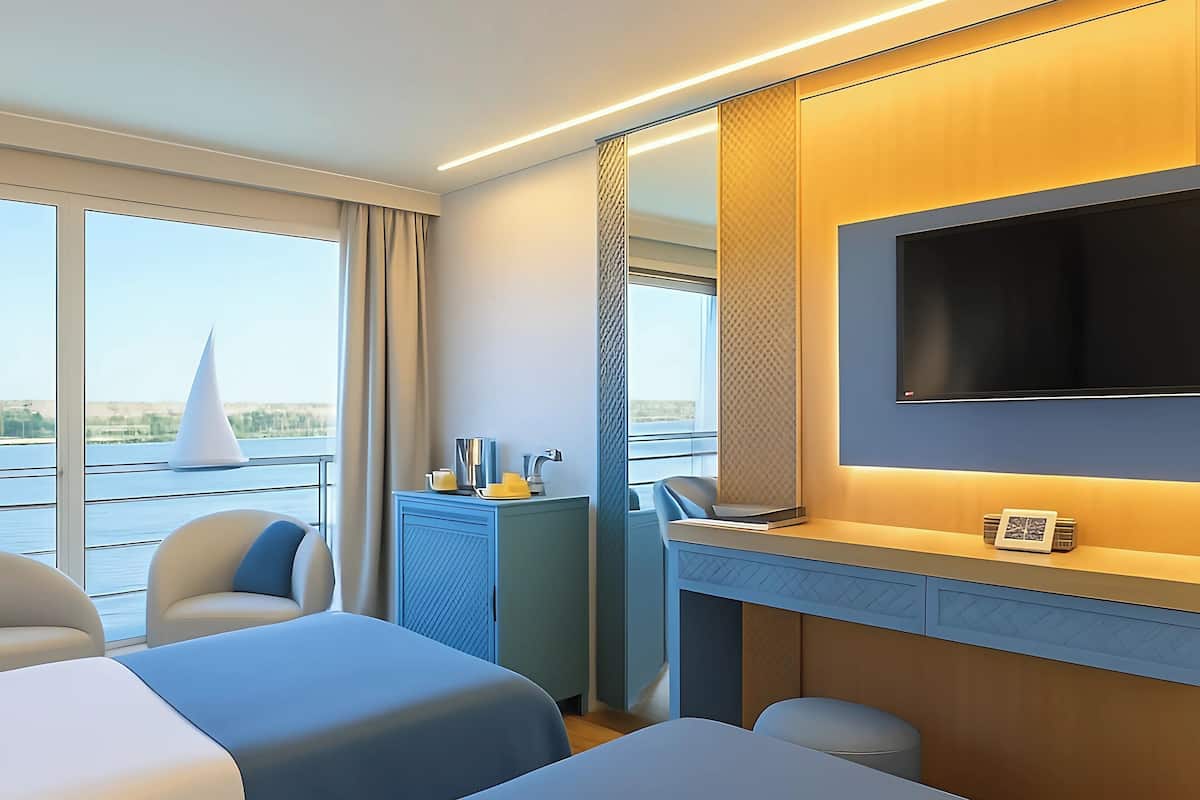 A hotel room with two beds, a desk with a flat-screen TV, a mirror, and a view of the water outside.