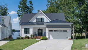 A two-story house with a garage, a front porch, and a view of the water. - New! Lakefront 4BR, Kayaks, Paddleboards, Games (Littleton)
