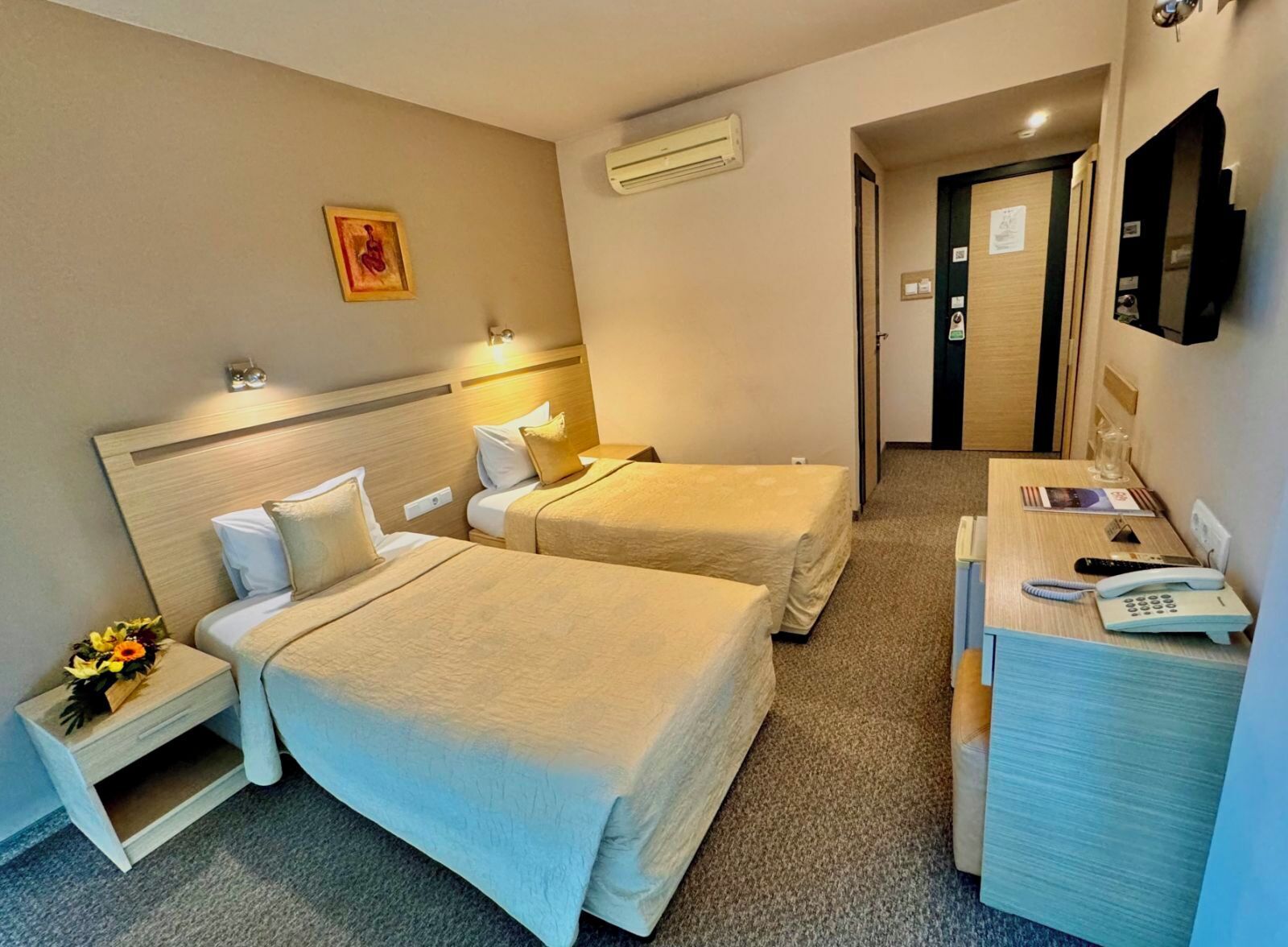 Une chambre d’hôtel avec deux lits, un bureau avec un téléphone et une petite table sur laquelle est posé un vase de fleurs.