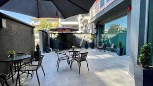 An outdoor patio area with round tables and chairs, umbrellas, and potted plants. - Expo Hotel (Plovdiv)