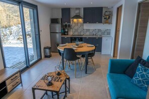A modern kitchen with a dining area, a blue sofa, and a table with a lamp.