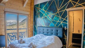 Een slaapkamer met een groot bed, uitzicht op bergen via een balkon, en een geometrisch wandontwerp.