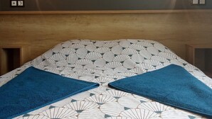 Quarto com cama, coberta estampada, cabeceira de madeira e prateleira sobre a cama.