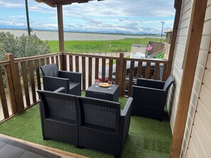 A balcony with wicker furniture, a grill, and a view of a river.