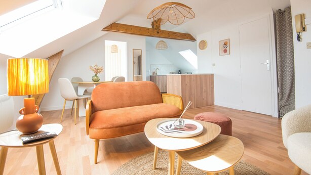 A modern living room with a sofa, coffee table, and lamp. There is a dining area with chairs and a table. A kitchen is visible in the background. - Cosy apartment in the heart of Angers (Angers)