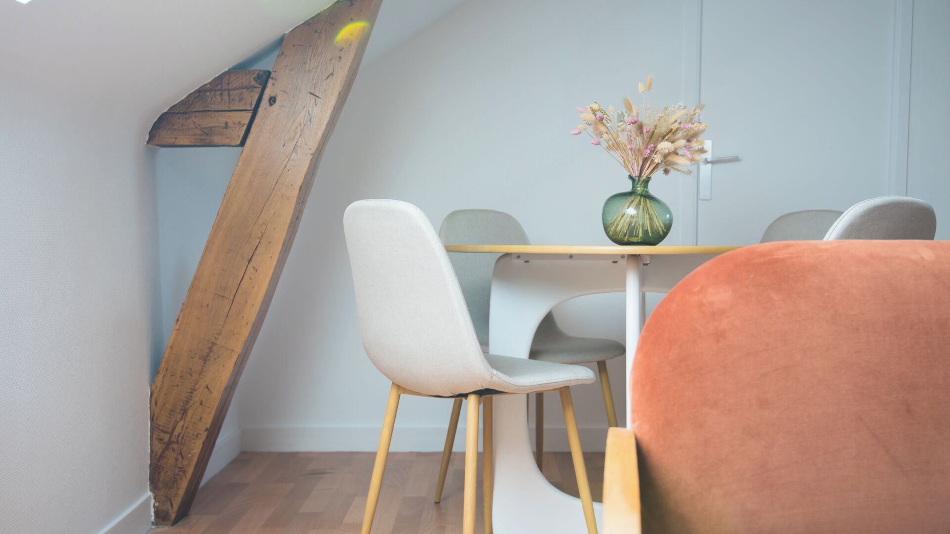 A dining area with a wooden beam, a table with chairs, and a vase with dried flowers.
