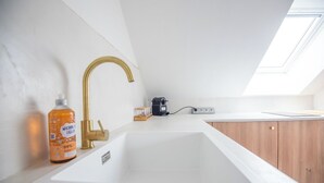A modern kitchen with a white sink, gold faucet, and wooden cabinets. - Cosy apartment in the heart of Angers (Angers)