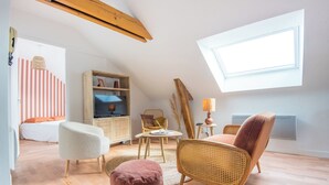 A cozy loft bedroom with a sloped ceiling, a large skylight, a television, a wicker chair, a cushioned ottoman, and a striped wall. - Cosy apartment in the heart of Angers (Angers)