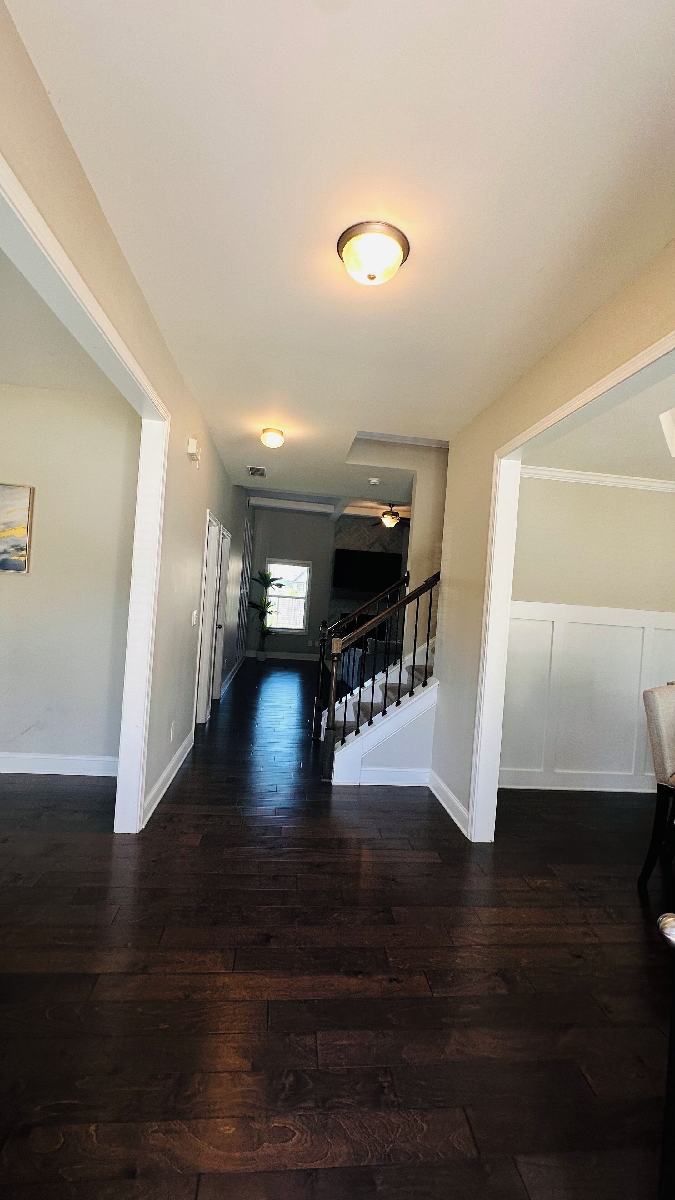 A spacious hallway with dark wooden floors, white walls, and a staircase leading to an upper level.