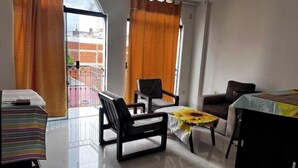 A modern living room with a sofa, chairs, a small table with a sunflower tablecloth, and a dining table.
