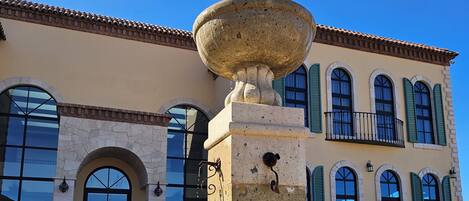 A building with a large stone fountain, arched windows, and a balcony with green shutters.