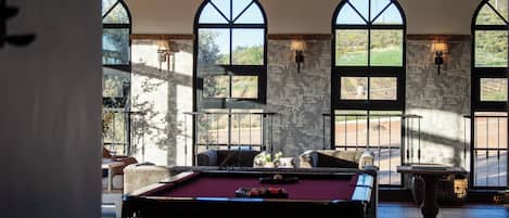 Una mesa de billar en una habitación con ventanas de arco y paredes de piedra.