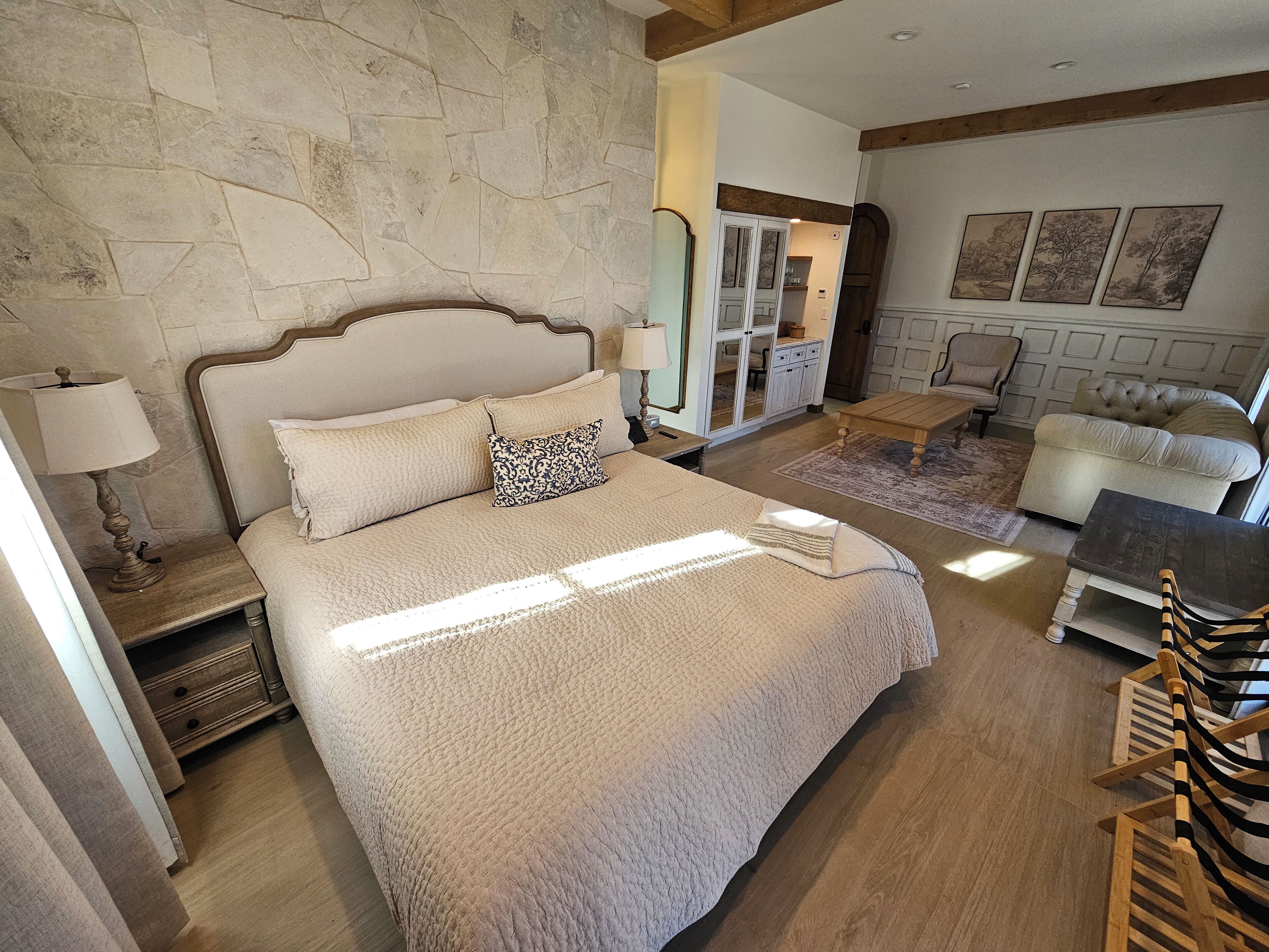 A bedroom with a large bed, a wooden nightstand, a bedside table, a chair, a sofa, and a dining table.