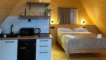 A cozy attic bedroom with a wooden sloped ceiling, a small kitchenette, and a bed with a headboard.