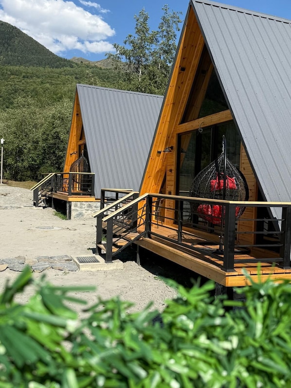 Two wooden cabins with metal roofs, each with a wooden deck and a staircase leading to the entrance. - Mestia POV Luxury Cabins (Mestia)