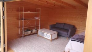 A compact room with a wooden ceiling, a grey sofa, a white coffee table, and a shelving unit against the wall.