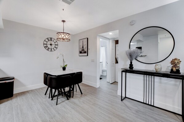 A modern interior with a dining area featuring a white table and black chairs, a console table with a mirror, and a decorative plant.