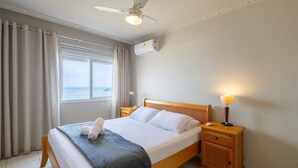 A hotel room with a bed, a nightstand, a lamp, a ceiling fan, and a window with curtains. - Apt w/ Balcony and Oceanfront View in BC - Ipc0901 (Balneário Camboriú)