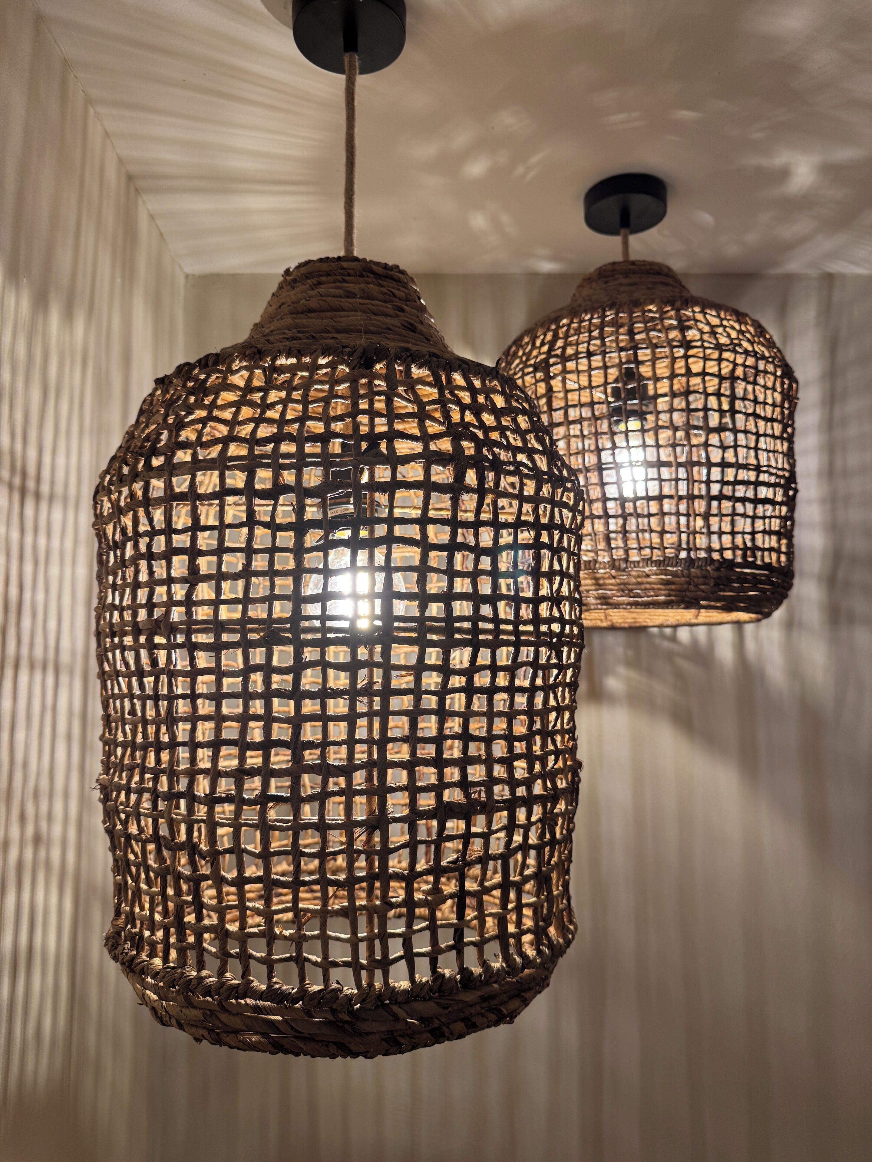 Two woven pendant lights hanging from the ceiling in a room with vertical striped wallpaper.
