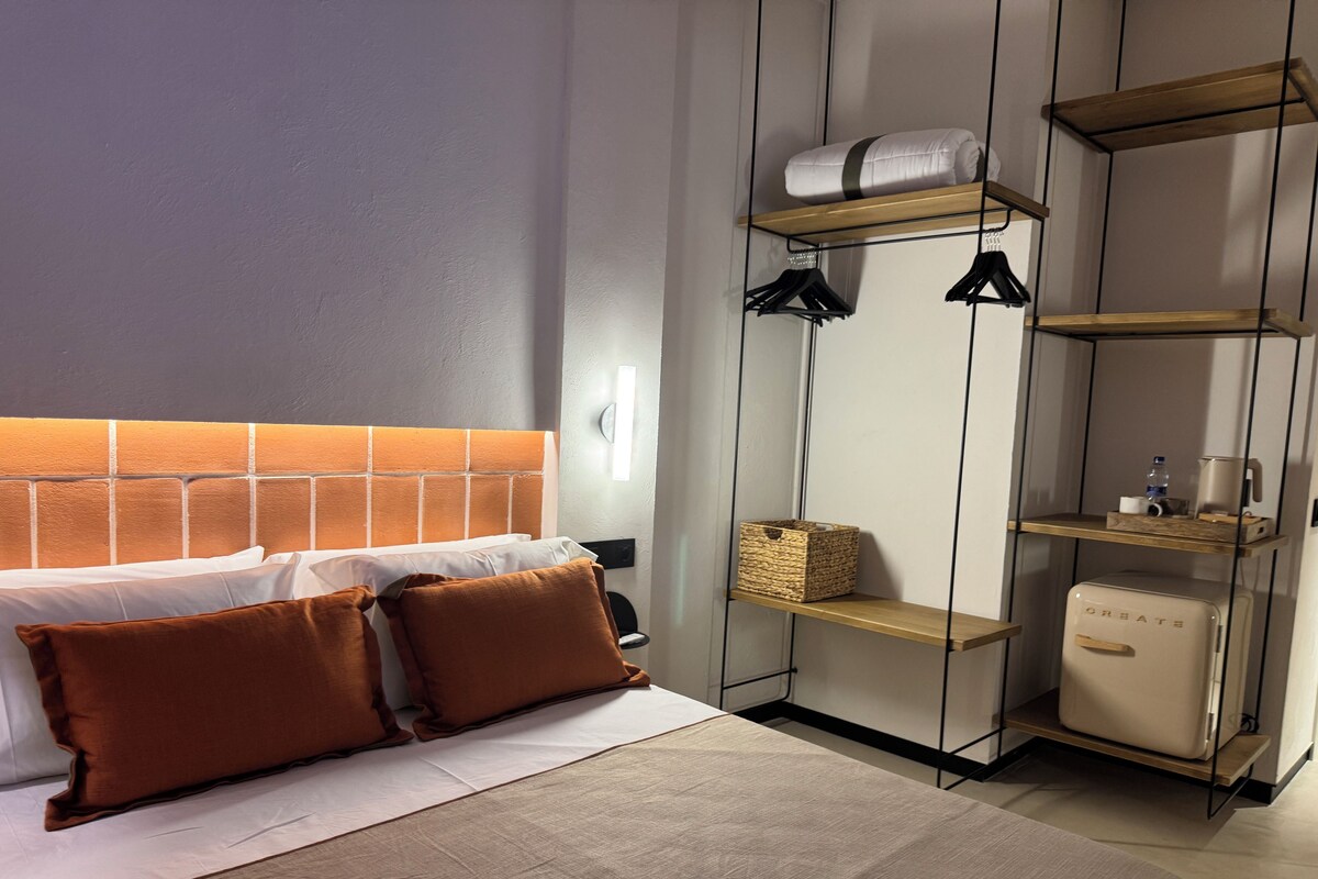 A neatly made bed with brown pillows, a headboard with a brick pattern, and a bedside table with a basket and a small appliance.