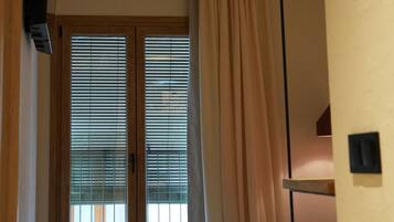Una habitación con ventilador de techo, una cama con edredón color beige, una ventana con persianas y una puerta con cortina.