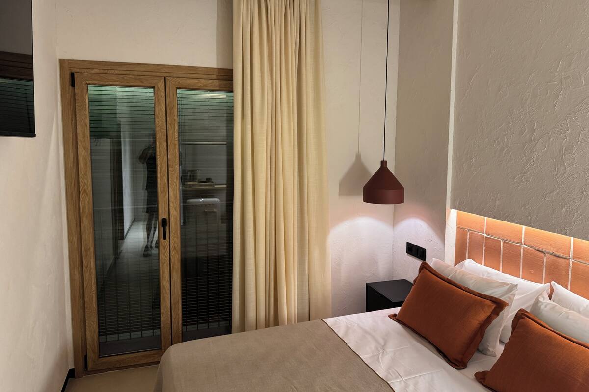 Une chambre d’hôtel comprenant un lit, une table de chevet, une suspension et une porte-fenêtre coulissante donnant sur une salle de bain.