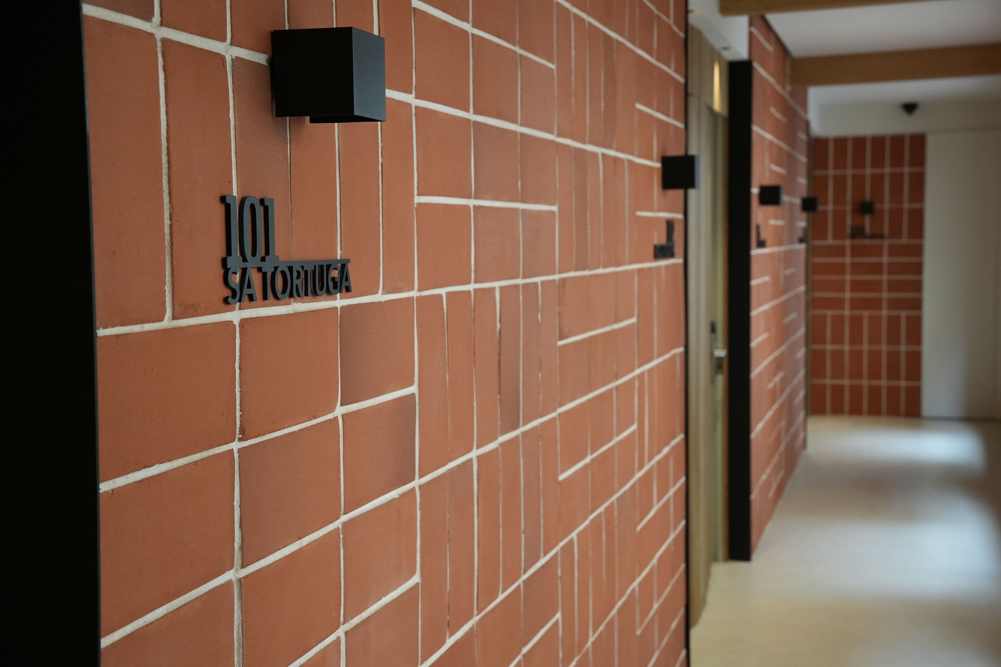 A hallway with a brick wall and a sign reading "101 SATORIUGA".