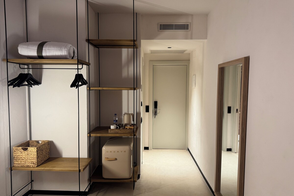 A modern, minimalist hallway with built-in shelving, a compact refrigerator, and a mirror reflecting the space.