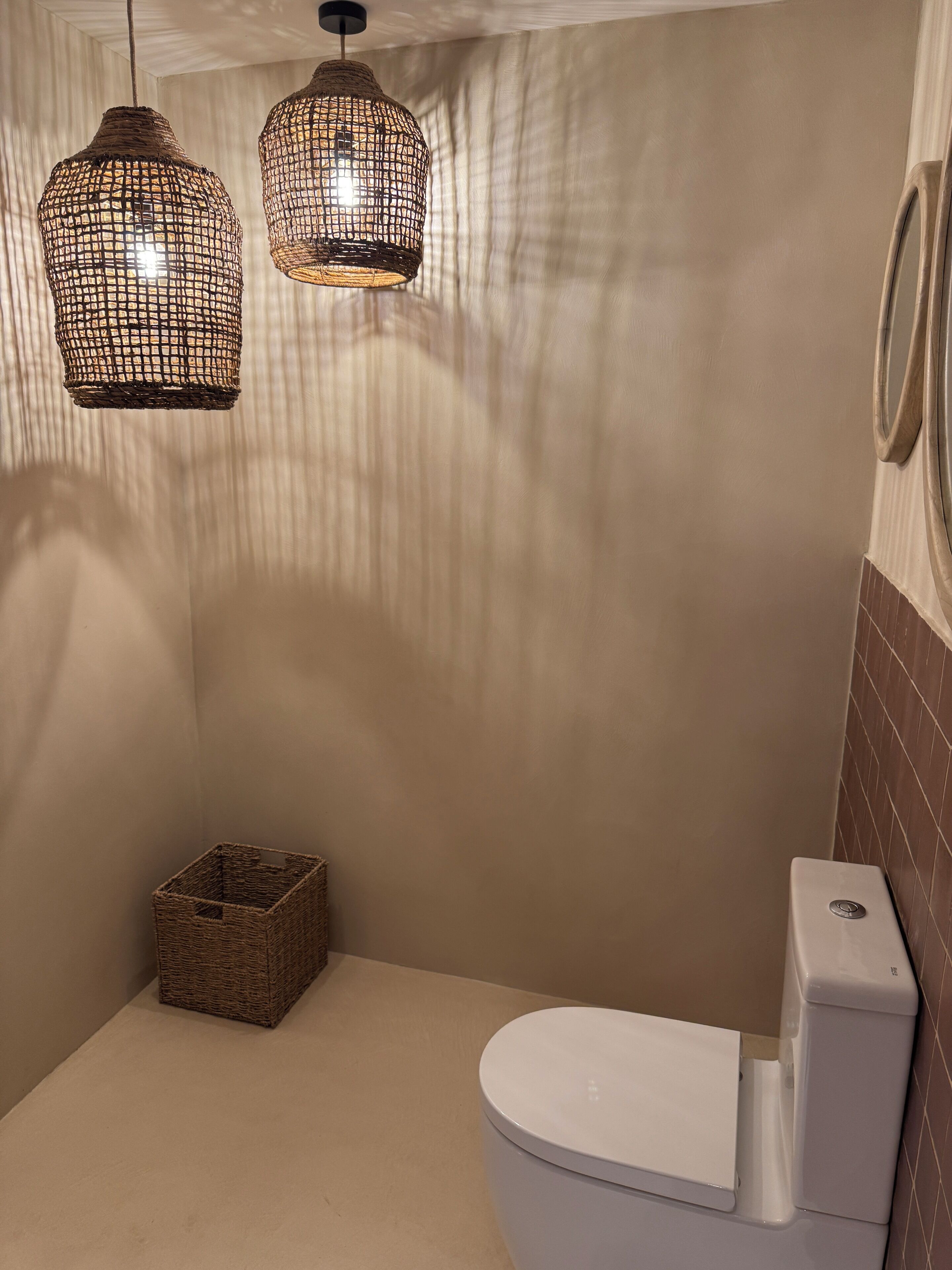Une salle de bain avec des toilettes, un panier en osier et deux suspensions en osier.