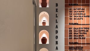 A wooden table in a room with a wall displaying a list of room numbers and names. - BELLADORA HOTEL BOUTIQUE (Lloret de Mar)