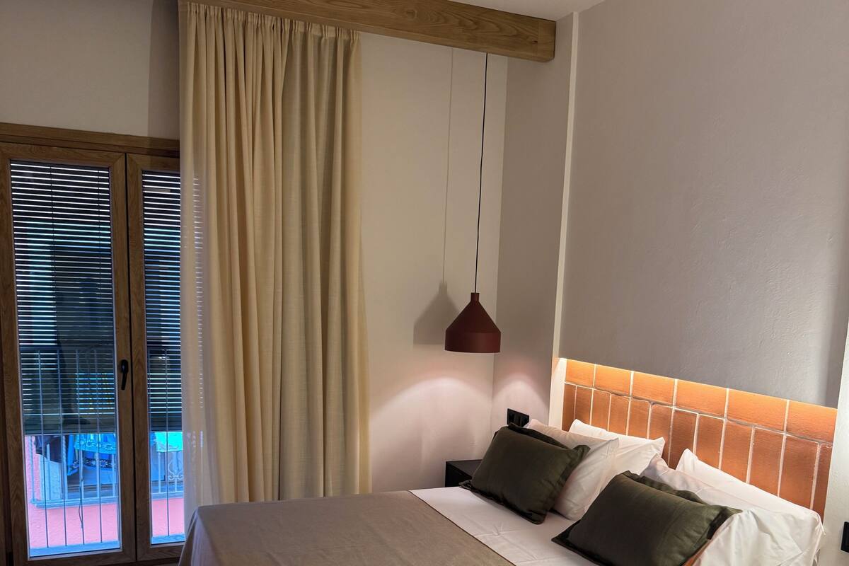 Une chambre d’hôtel avec un grand lit, un ventilateur de plafond, une vue sur l’extérieur grâce à une porte coulissante et un luminaire suspendu.