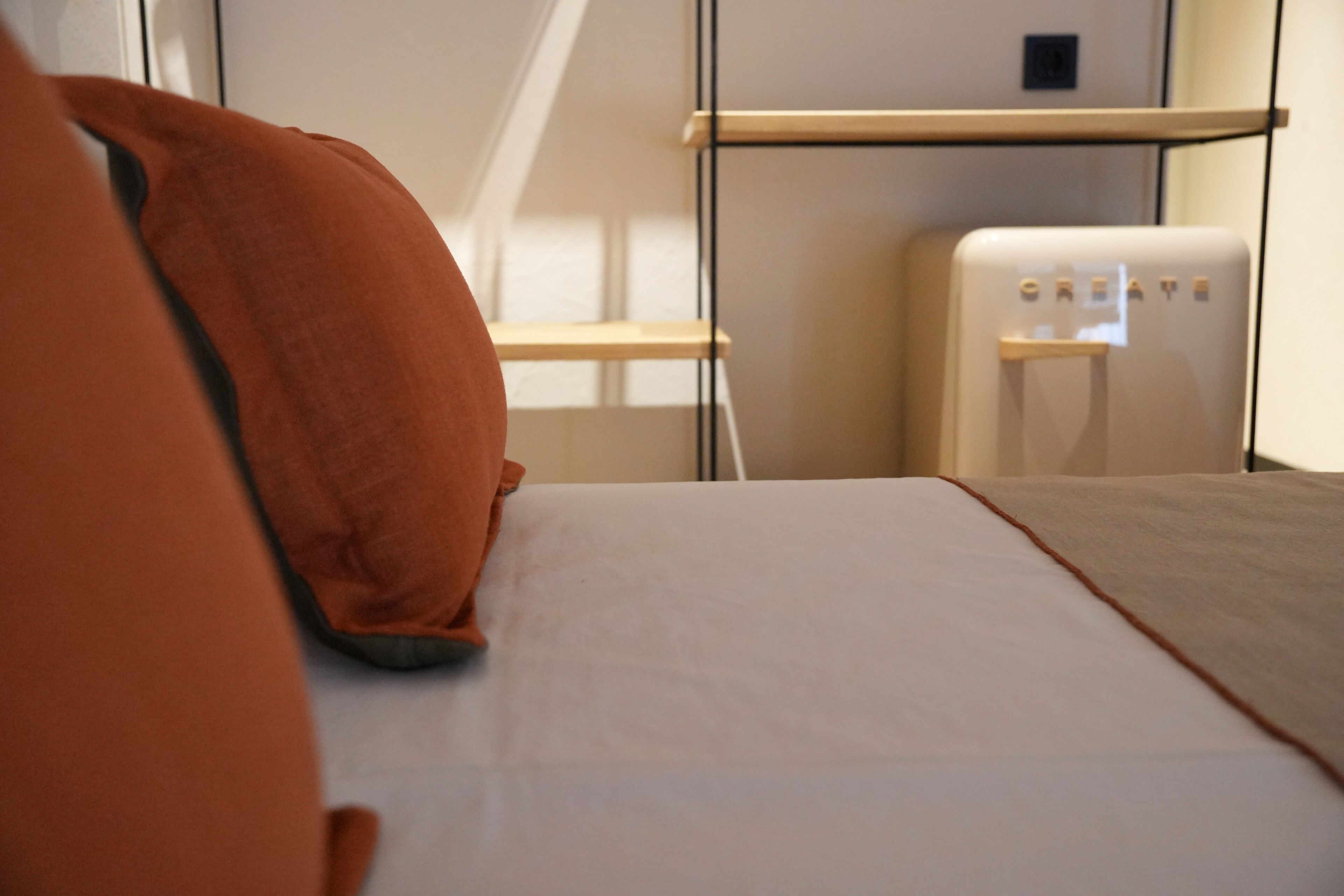A modern hotel room with a bed, a white wall, and a small white appliance labeled "CREATE".